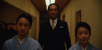 Movie still from “Tokyo Vice” (2022), created by J.T. Rogers – A man wearing a suit and tie standing in a hallway; Medium shot, Low angle