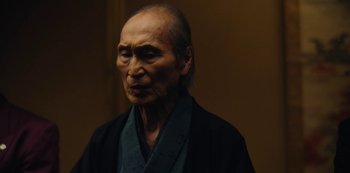 Movie still from “Tokyo Vice” (2022), created by J.T. Rogers – An older man wearing a black robe looking at the camera; Close Up shot, Low angle