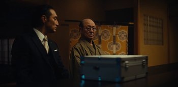 Movie still from “Tokyo Vice” (2022), created by J.T. Rogers – A man in glasses and a robe standing next to another man; Medium shot, Over the shoulder angle