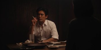 Movie still from “Tokyo Vice” (2022), created by J.T. Rogers – A man sitting at a table with a cigarette in his mouth; Medium shot, Over the shoulder angle
