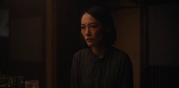 Movie still from “Tokyo Vice” (2022), created by J.T. Rogers – A woman in a dark room looking at the camera; Close Up shot, Over the shoulder angle