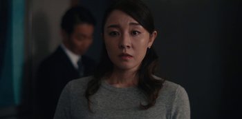 Movie still from “Tokyo Vice” (2022), created by J.T. Rogers – A woman in a gray shirt is standing in front of a man in a black suit; Close Up shot, Over the shoulder angle