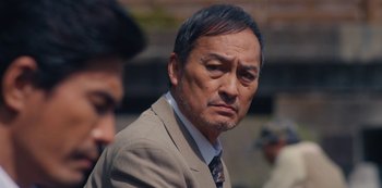 Movie still from “Tokyo Vice” (2022), created by J.T. Rogers – An asian man in a suit and tie; Close Up shot, Over the shoulder angle