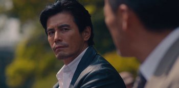 Movie still from “Tokyo Vice” (2022), created by J.T. Rogers – A person wearing a suit and tie; Close Up shot, Over the shoulder angle