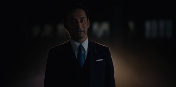Movie still from “Tokyo Vice” (2022), created by J.T. Rogers – A man wearing a suit and tie standing in the dark; Close Up shot, Low angle