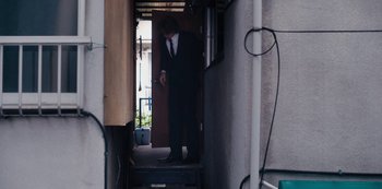 Movie still from “Tokyo Vice” (2022), created by J.T. Rogers – A man wearing a suit and tie standing in a doorway; Wide shot, Low angle