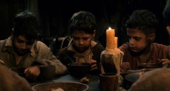 Movie still from “Tom Thumb” (2001), directed by Olivier Dahan – A group of people sitting around a table with a candle; Medium shot, Low angle