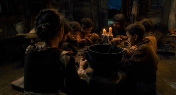 Movie still from “Tom Thumb” (2001), directed by Olivier Dahan – A group of people sitting around a table with candles on it; Medium shot, High angle