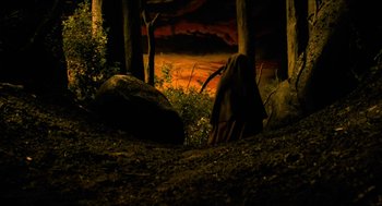 Movie still from “Tom Thumb” (2001), directed by Olivier Dahan – A dark forest with a rock and trees in the background; Wide shot, High angle