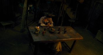 Movie still from “Tom Thumb” (2001), directed by Olivier Dahan – A person sitting at a table with a candle; Wide shot, Overhead angle