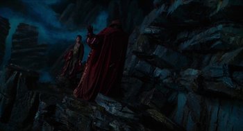 Movie still from “Tom Thumb” (2001), directed by Olivier Dahan – Two men in red robes standing next to a rock wall; Wide shot, High angle