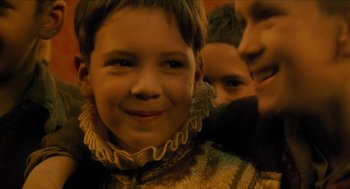 Movie still from “Tom Thumb” (2001), directed by Olivier Dahan – A young boy smiling with two other people behind him; Close Up shot, Over the shoulder angle