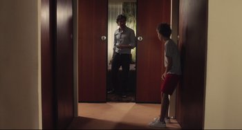 Movie still from “Tomboy” (2011), directed by Céline Sciamma – A man standing in front of a mirror while another man stands in front of a door; Wide shot, Over the shoulder angle