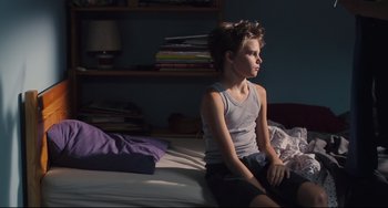 Movie still from “Tomboy” (2011), directed by Céline Sciamma – A boy sitting on a bed in a room; Medium shot, High angle