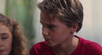 Movie still from “Tomboy” (2011), directed by Céline Sciamma – A young boy looking to his left while wearing a red t - shirt; Close Up shot, Over the shoulder angle