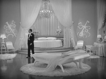Movie still from “Top Hat” (1935), directed by Mark Sandrich – A black and white photo of a man standing in front of a bed; Wide shot, High angle
