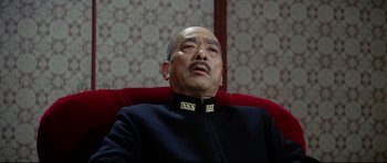 Movie still from “Tora! Tora! Tora!” (1970), directed by Kinji Fukasaku – An older man sitting in a red chair wearing a black jacket; Close Up shot, Low angle