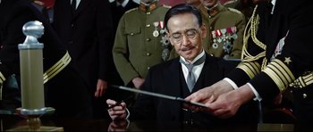 Movie still from “Tora! Tora! Tora!” (1970), directed by Kinji Fukasaku – A man in a suit and tie holding a cell phone; Medium shot, Low angle