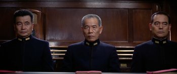 Movie still from “Tora! Tora! Tora!” (1970), directed by Kinji Fukasaku – An older man sitting in front of a wooden wall; Medium shot, Low angle