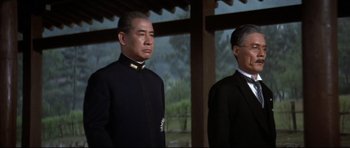 Movie still from “Tora! Tora! Tora!” (1970), directed by Kinji Fukasaku – A man in a suit and tie standing next to another man in a suit and tie; Medium shot, Low angle