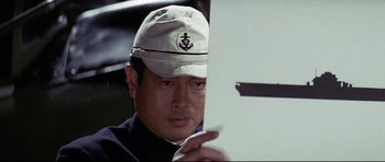 Movie still from “Tora! Tora! Tora!” (1970), directed by Kinji Fukasaku – A man wearing a white hat and holding a white board; Close Up shot, Over the shoulder angle