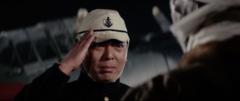 Movie still from “Tora! Tora! Tora!” (1970), directed by Kinji Fukasaku – A man wearing a hat saluting in front of a crowd; Close Up shot, Low angle