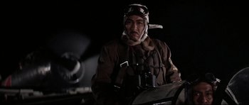 Movie still from “Tora! Tora! Tora!” (1970), directed by Kinji Fukasaku – A man in a brown jacket wearing a hat and holding binoculars in front of an airplane; Close Up shot, Low angle