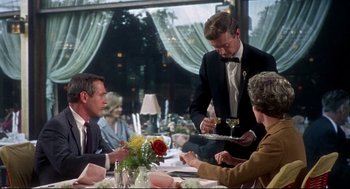 Movie still from “Torn Curtain” (1966), directed by Alfred Hitchcock – A man in a suit is serving a plate of food to a woman; Medium shot, Over the shoulder angle