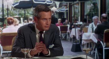 Movie still from “Torn Curtain” (1966), directed by Alfred Hitchcock – A man sitting at a table in front of some people; Close Up shot, Over the shoulder angle