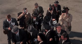 Movie still from “Torn Curtain” (1966), directed by Alfred Hitchcock – A group of men in suits and hats taking pictures; Wide shot, High angle