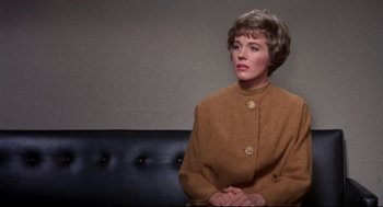 Movie still from “Torn Curtain” (1966), directed by Alfred Hitchcock – A woman sitting on a couch in front of a wall; Medium shot, Over the shoulder angle