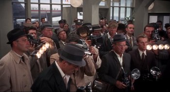 Movie still from “Torn Curtain” (1966), directed by Alfred Hitchcock – A group of men in suits and hats taking pictures; Wide shot, High angle