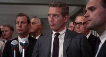 Movie still from “Torn Curtain” (1966), directed by Alfred Hitchcock – A man in a suit and tie standing in front of a microphone; Close Up shot, Low angle