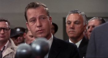 Movie still from “Torn Curtain” (1966), directed by Alfred Hitchcock – A man in a suit and tie standing next to a microphone; Close Up shot, Low angle