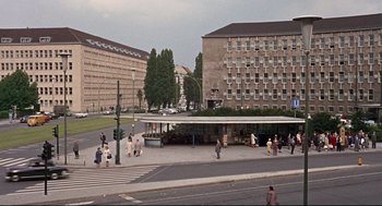 Movie still from “Torn Curtain” (1966), directed by Alfred Hitchcock – A group of people standing on the side of a road near a building; Extreme Wide shot, High angle