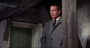 Movie still from “Torn Curtain” (1966), directed by Alfred Hitchcock – A man in a suit and tie standing next to a wooden post; Medium shot, Low angle