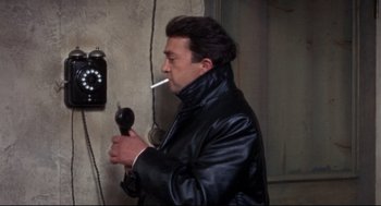 Movie still from “Torn Curtain” (1966), directed by Alfred Hitchcock – A man smoking a cigarette while holding a hair dryer; Close Up shot, High angle