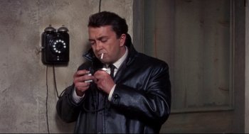Movie still from “Torn Curtain” (1966), directed by Alfred Hitchcock – A man smoking a cigarette while looking at a phone; Close Up shot, High angle