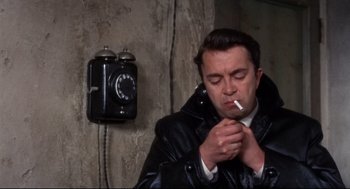 Movie still from “Torn Curtain” (1966), directed by Alfred Hitchcock – A man smoking a cigarette in front of an old phone; Close Up shot, Low angle