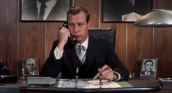 Movie still from “Torn Curtain” (1966), directed by Alfred Hitchcock – A man sitting at a desk talking on a phone; Medium shot, Low angle