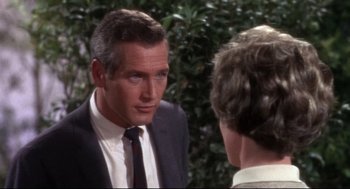 Movie still from “Torn Curtain” (1966), directed by Alfred Hitchcock – A man in a suit talking to a woman in front of a bush; Close Up shot, Over the shoulder angle