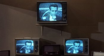 Movie still from “Torn Curtain” (1966), directed by Alfred Hitchcock – Three televison screens with a man on a television screen; Medium shot, High angle