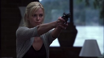 A beautiful blonde woman holding a gun in a room