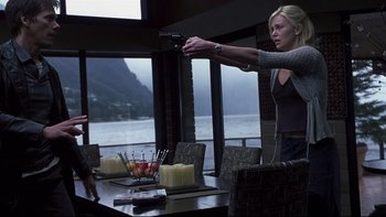 Movie still from “Trapped” (2002), directed by Luis Mandoki – A woman holding a gun in front of a table; Medium shot, Over the shoulder angle