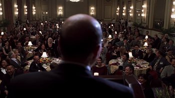 Movie still from “Trapped” (2002), directed by Luis Mandoki – A man standing in front of a room full of people; Medium shot, Over the shoulder angle