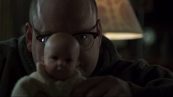 Movie still from “Trapped” (2002), directed by Luis Mandoki – A man holding a baby doll in his hands; Close Up shot, Over the shoulder angle