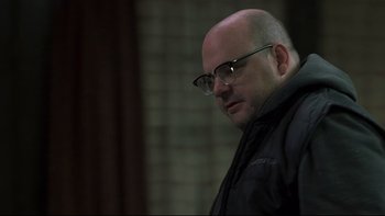 Movie still from “Trapped” (2002), directed by Luis Mandoki – A bald man with glasses is looking down; Close Up shot, Low angle