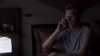 Movie still from “Trapped” (2002), directed by Luis Mandoki – A man sitting on a couch talking on a cell phone; Medium shot, High angle