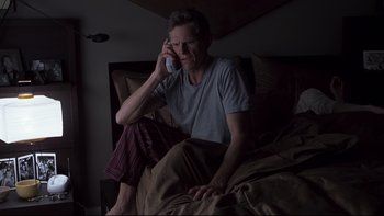 Movie still from “Trapped” (2002), directed by Luis Mandoki – A man sitting on a bed talking on a phone; Medium shot, High angle