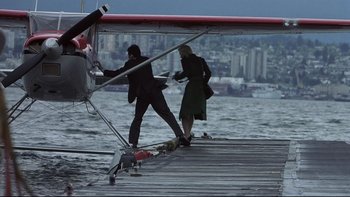Movie still from “Trapped” (2002), directed by Luis Mandoki – A man and a woman standing next to a water plane; Wide shot, Low angle